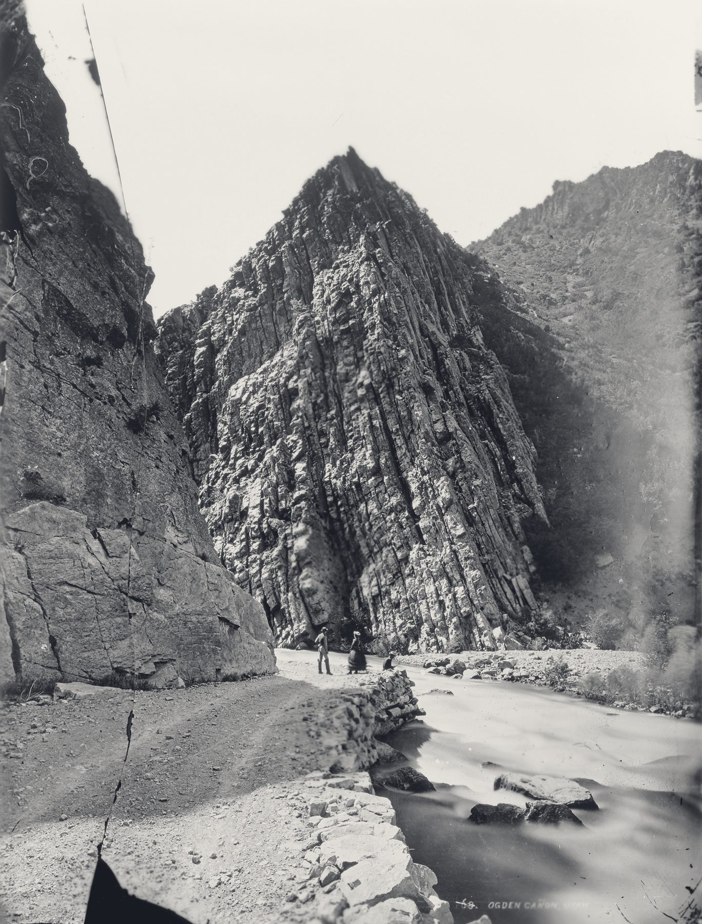 An 1871 photograph of a narrow road and river beneath the towering cliffs of Ogden Canyon