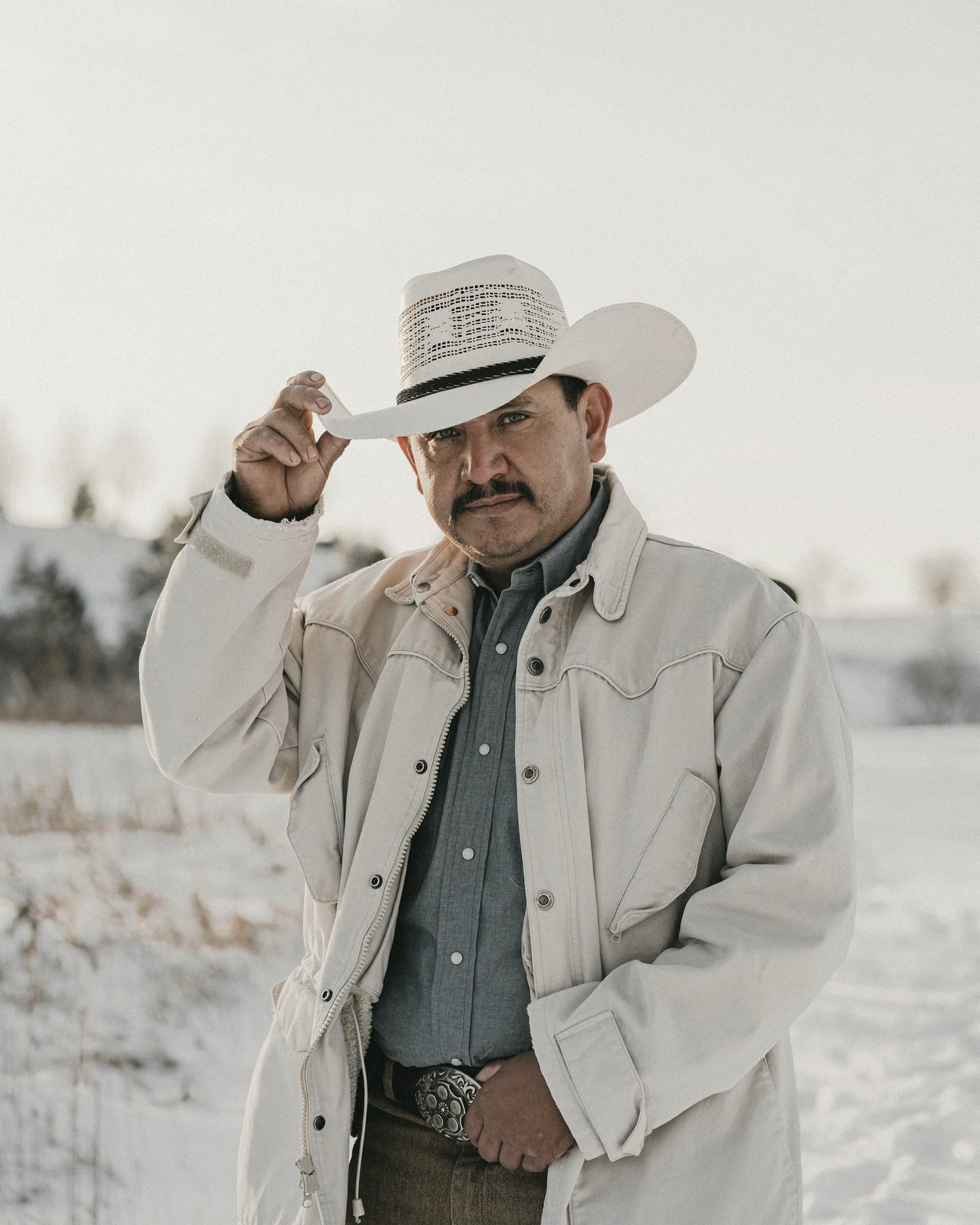 A rancher in a white hat and canvas jacket stands in a snowy field