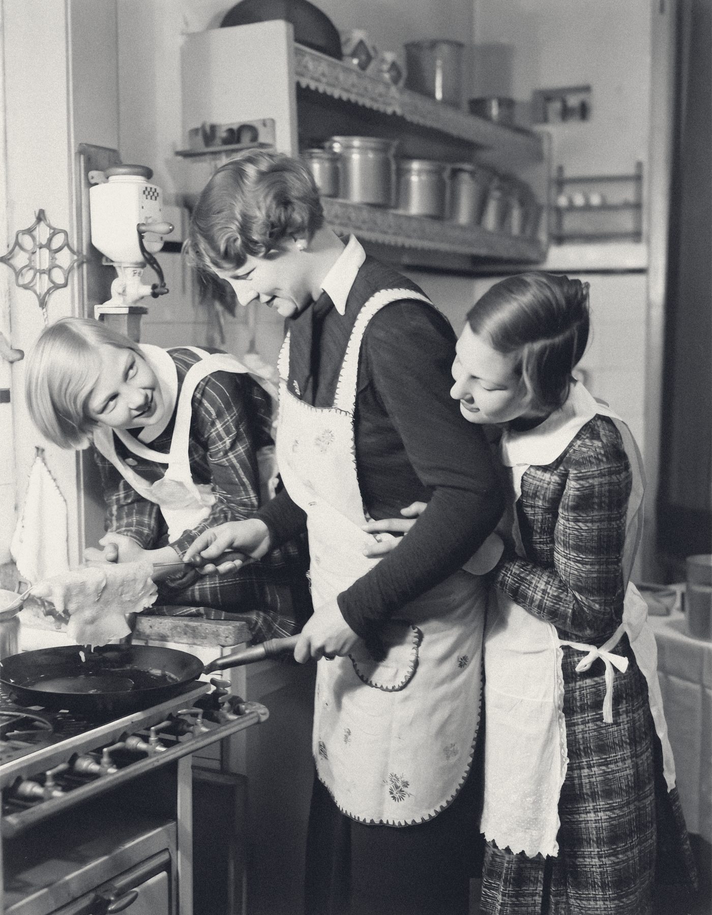 A vintage photograph of a mother and two daughters cooking together