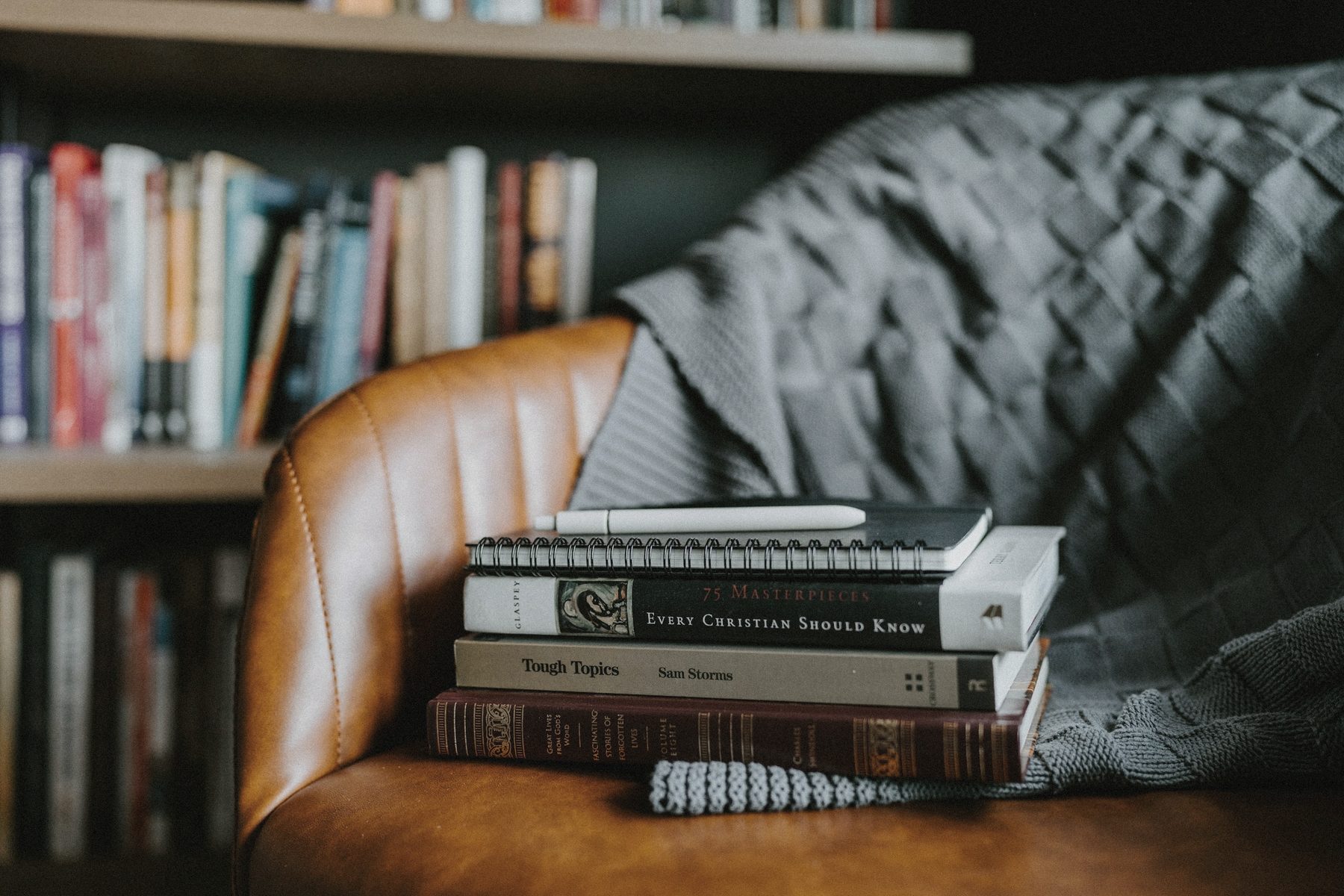 A stack of well-worn books resting on a leather armchair in a library